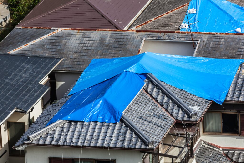 Houses with tiled roof covered by blue sheet after hurricane storm damage repair berry roofing