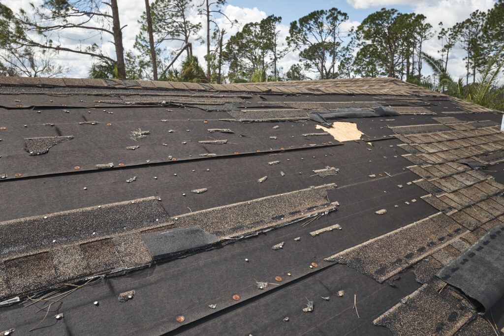Wind damaged house roof with missing asphalt shingles after hurricane Ian in Florida. Repair of home rooftop riverside